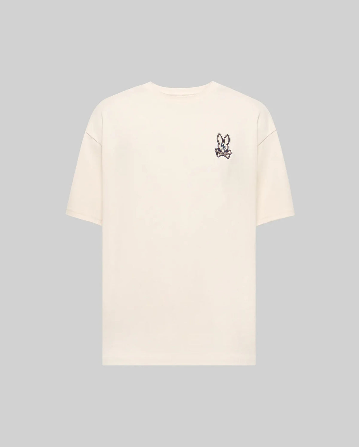 The Psycho Bunny MENS WADE OVERSIZED FIT CHEST TEE - MT0200152 is a plain beige Pima cotton tee with a small cartoon bunny face patch on the left chest, shown against a light gray background.