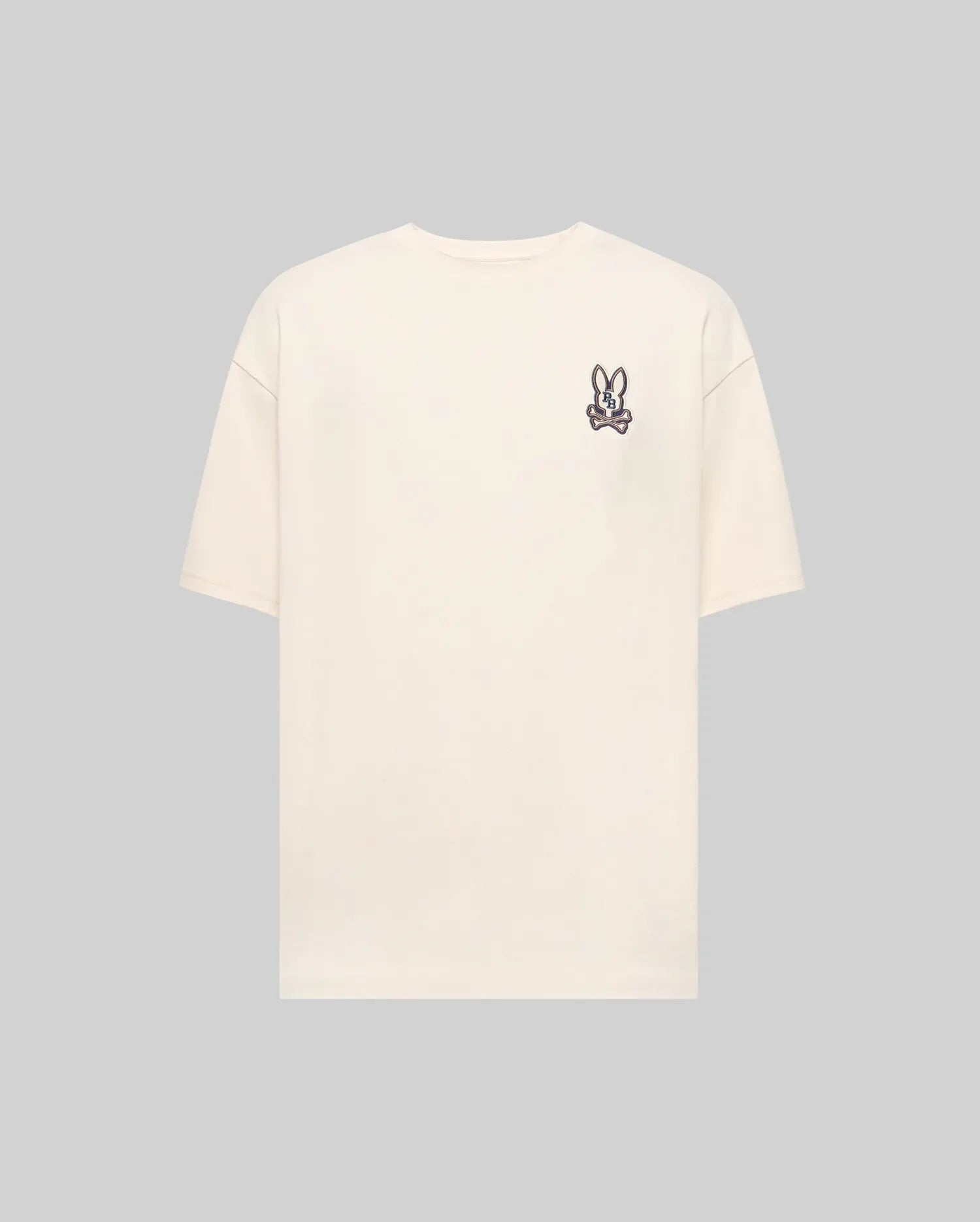The Psycho Bunny MENS WADE OVERSIZED FIT CHEST TEE - MT0200152 is a plain beige Pima cotton tee with a small cartoon bunny face patch on the left chest, shown against a light gray background.