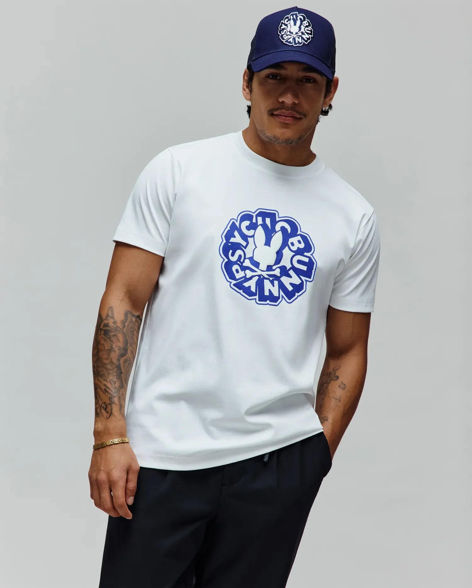 Mens Toby Graphic Tee, a classic fit white jersey t-shirt featuring a large central blue Psycho Bunny skull and crossbones logo within a circular graphic text design.