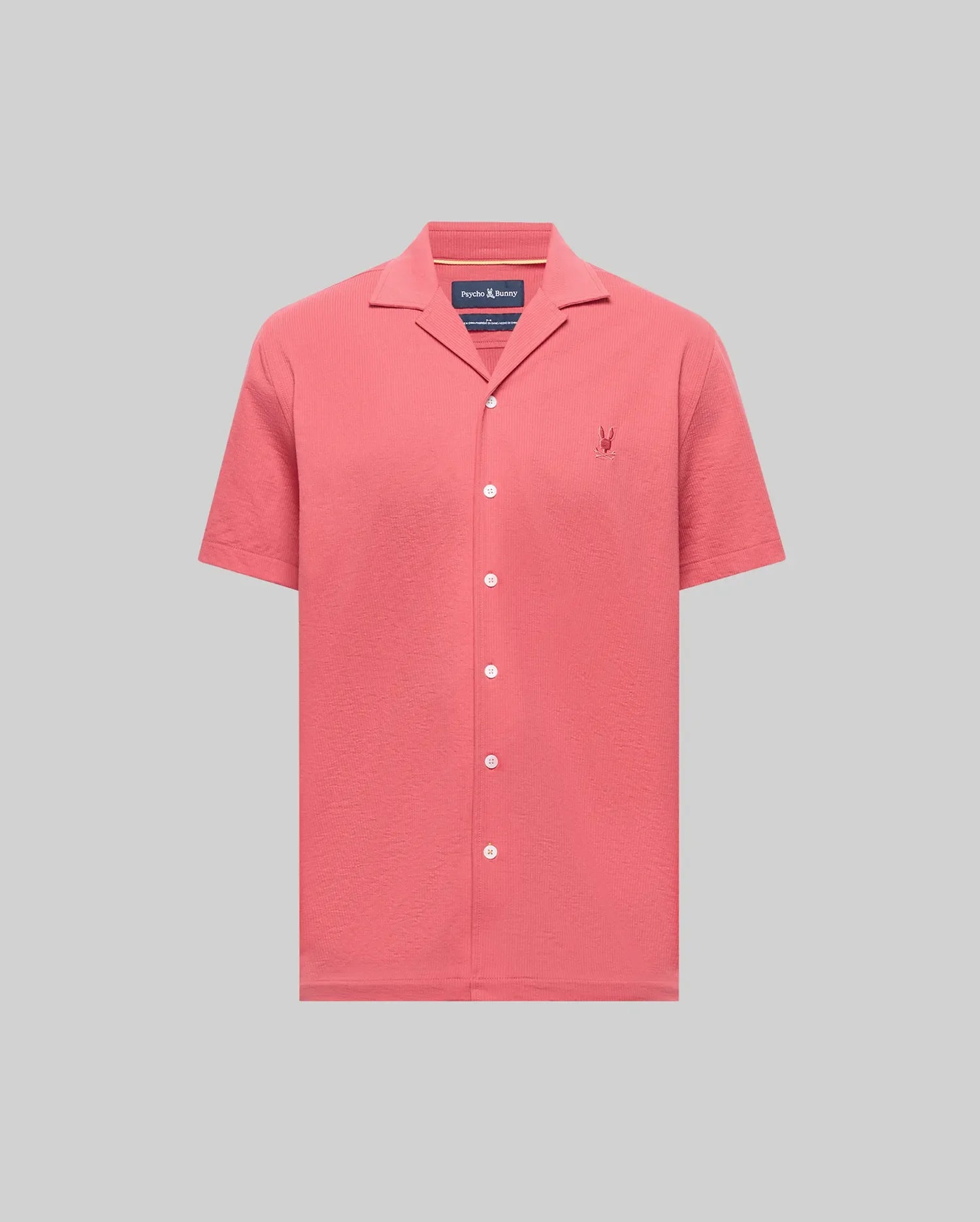 The PsychoBunny MENS JAYME KNIT SEERSUCKER CABANA COLLAR SHIRT (MT0300002) is a short-sleeved, button-up in coral pink with a cabana collar and embroidered logo, crafted from a premium cotton blend and shown on a light grey background.
