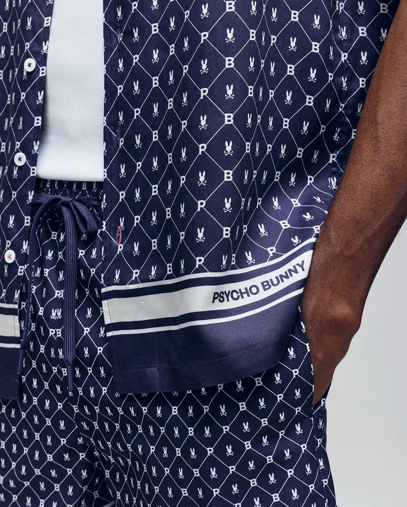 A person wears the Psycho Bunny MENS HUNTER TENCEL SHIRT - MT0300016, a navy blue breathable set with a white bunny logo pattern and “PSYCHO BUNNY” text near the hem; their hand is in their pocket.