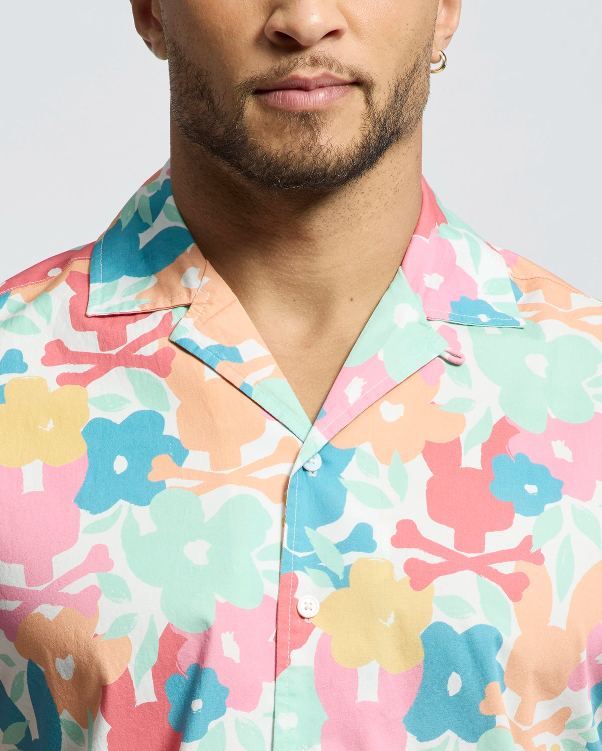 A person wears the Psycho Bunny MENS MEYLON STRETCH POPLIN SHIRT - MT0300034, featuring a colorful floral pattern. Only the lower half of their face and upper torso are visible.