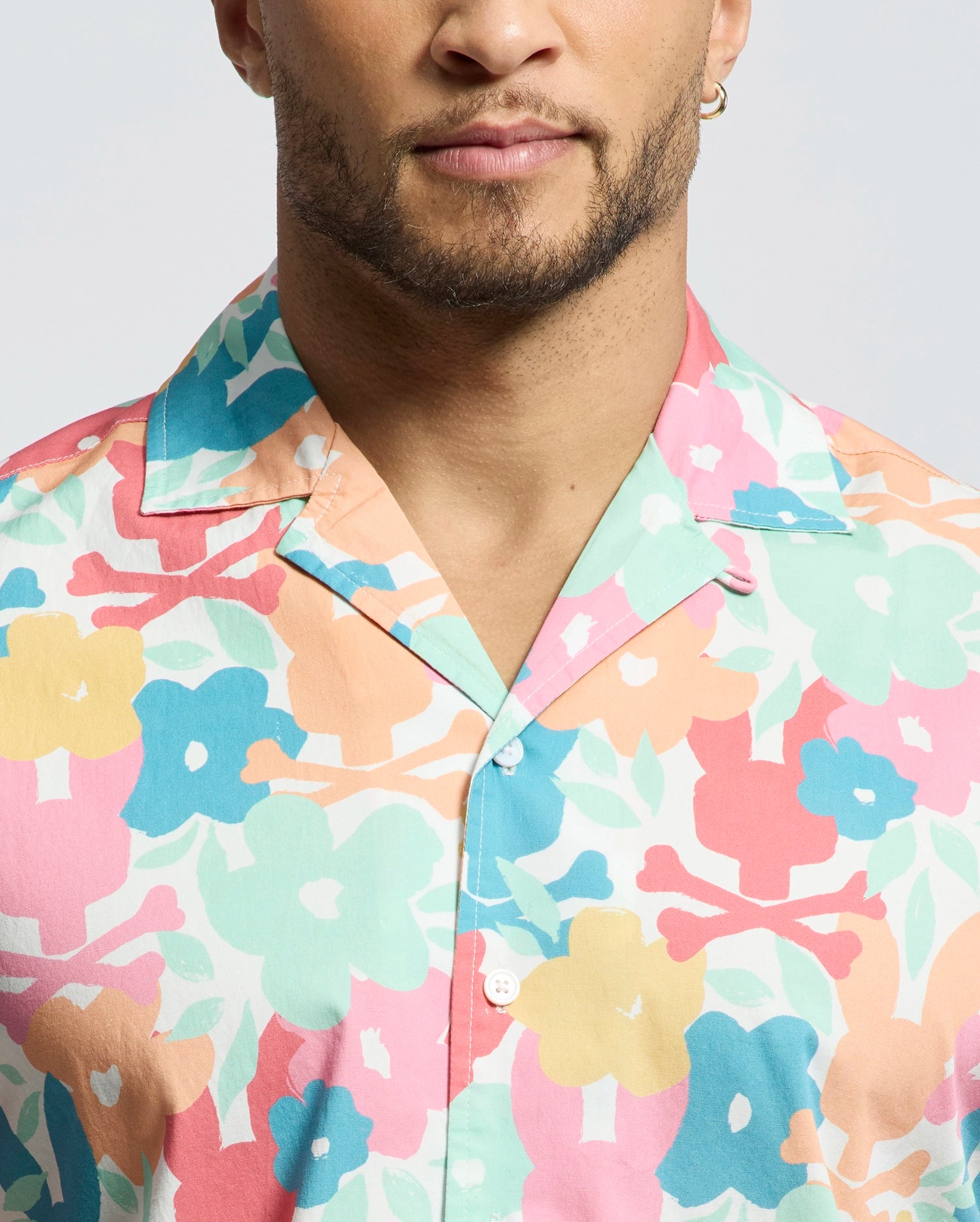 A person wears the Psycho Bunny MENS MEYLON STRETCH POPLIN SHIRT - MT0300034, featuring a colorful floral pattern. Only the lower half of their face and upper torso are visible.