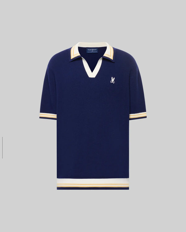 The Psycho Bunny MENS CARTER JOHNNY COLLAR KNIT POLO (MT0400093) is a navy blue cotton short-sleeve shirt with white and beige striped collar, cuffs, and hem, plus a white embroidered bird logo on the left chest. Regular fit.