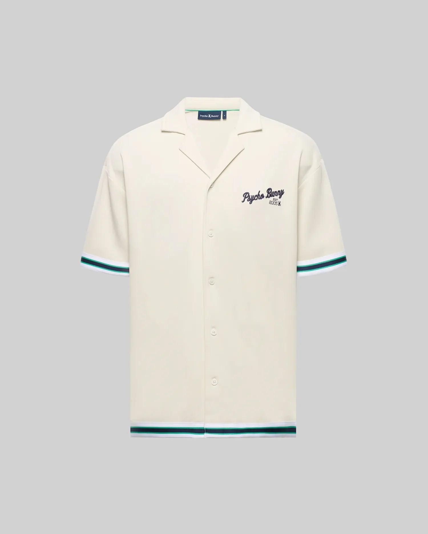 The Psycho Bunny MENS BASIL TAPED CAMP COLLAR SHIRT (MT0500004) is a cream, short-sleeve shirt with a Johnny collar, teal and black striped sleeves and hem, embroidered "Psycho Bunny" on the chest, made from cotton-modal blend. Shown on gray.
