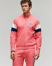 A man stands facing forward in a Psycho Bunny MENS DAWSON 1/4 COLORBLOCKED SWEATSHIRT (MT0500113), a pink cotton-modal blend with navy and white sleeve stripes and a bunny skull logo, set against a plain gray background for an athletic style.