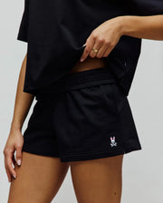 Womens Olivia Fleece Short, black relaxed-fit French terry shorts featuring a small embroidered Psycho Bunny skull logo with pink ears on the left leg hem.