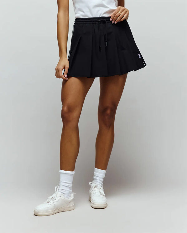 Womens Cecilia Pleated Skort in black, featuring a classic fit, smooth fabric, white side stripe, drawstring waist, and a small embroidered purple Psycho Bunny skull logo on the lower left front.