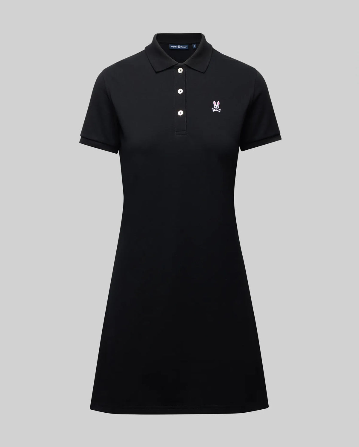 The WOMENS POLO DRESS - WO2000003 by Psycho Bunny is a black Pima polo dress with a collar, three white buttons, and a small white Bunny logo on the chest, shown on a plain gray background.