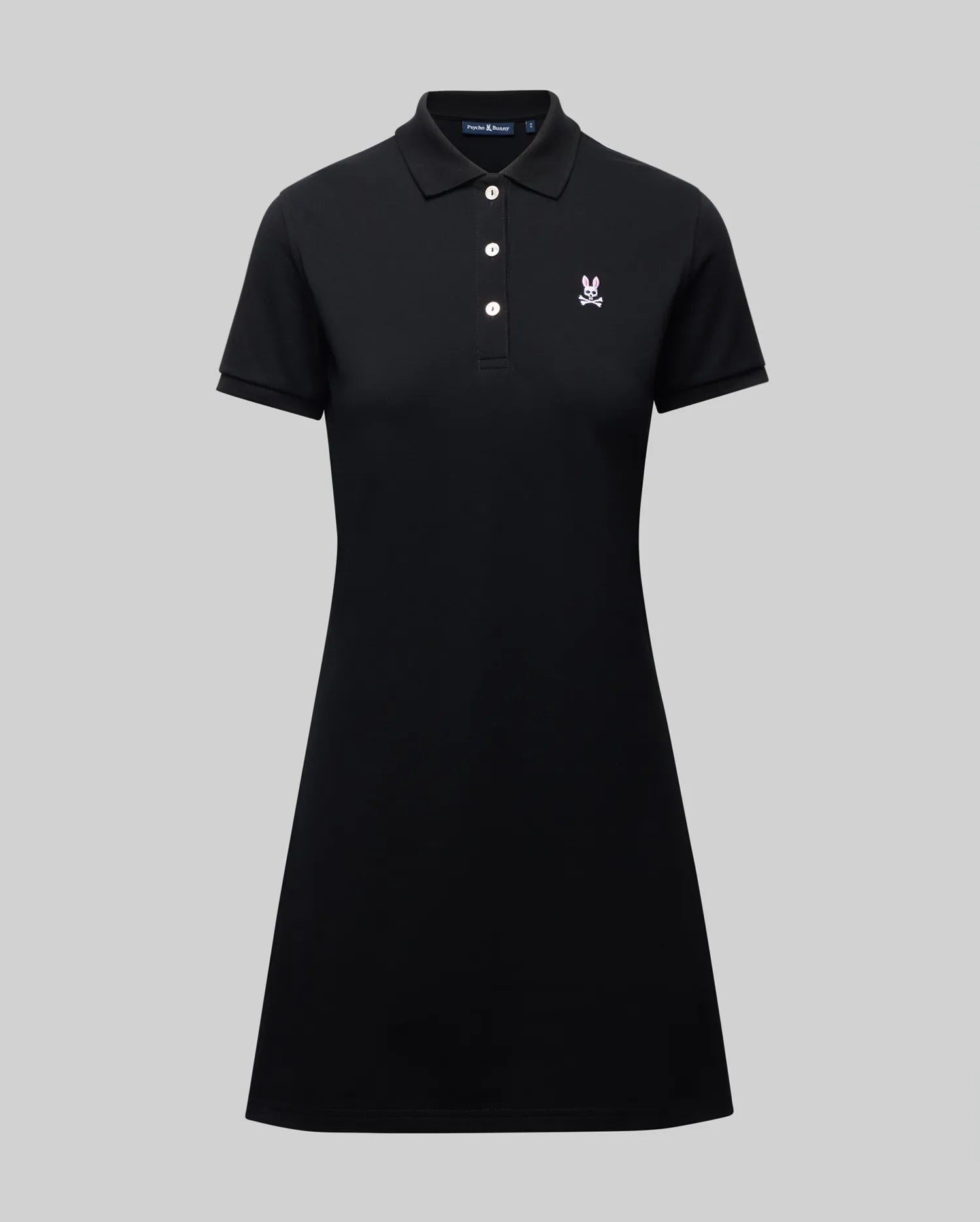 The WOMENS POLO DRESS - WO2000003 by Psycho Bunny is a black Pima polo dress with a collar, three white buttons, and a small white Bunny logo on the chest, shown on a plain gray background.