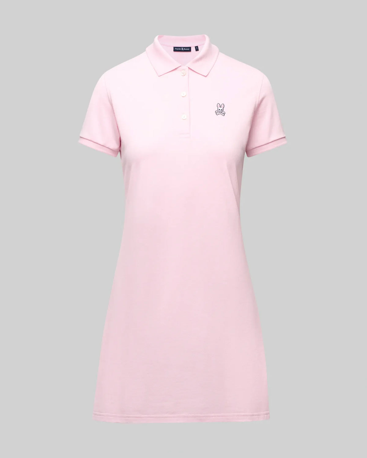 The Psycho Bunny WOMENS POLO DRESS - WO2000003 is a light pink Pima polo dress with a feminine fit, collar, three Mother-of-Pearl buttons, and a small embroidered bunny logo on the left chest, shown on a plain gray background.