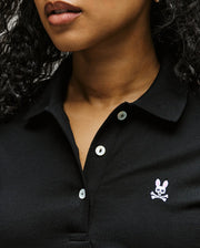 A close-up of a woman in the Psycho Bunny WOMENS PIQUE POLO - WT0100003, featuring white buttons and a 4k-stitch embroidered Bunny skull and crossbones logo; only her lips and lower face are visible.
