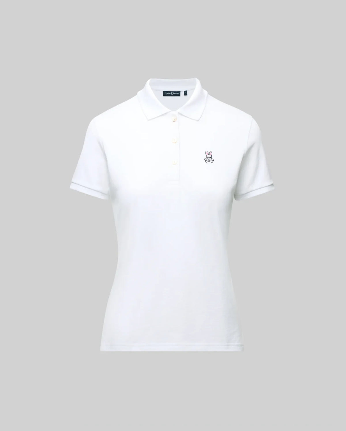 The WOMENS PIQUE POLO - WT0100003 by Psycho Bunny is a white pique polo featuring a collar, buttons, and the embroidered Bunny logo on the left chest. Crafted for Pima flexibility, it is presented against a plain grey background.