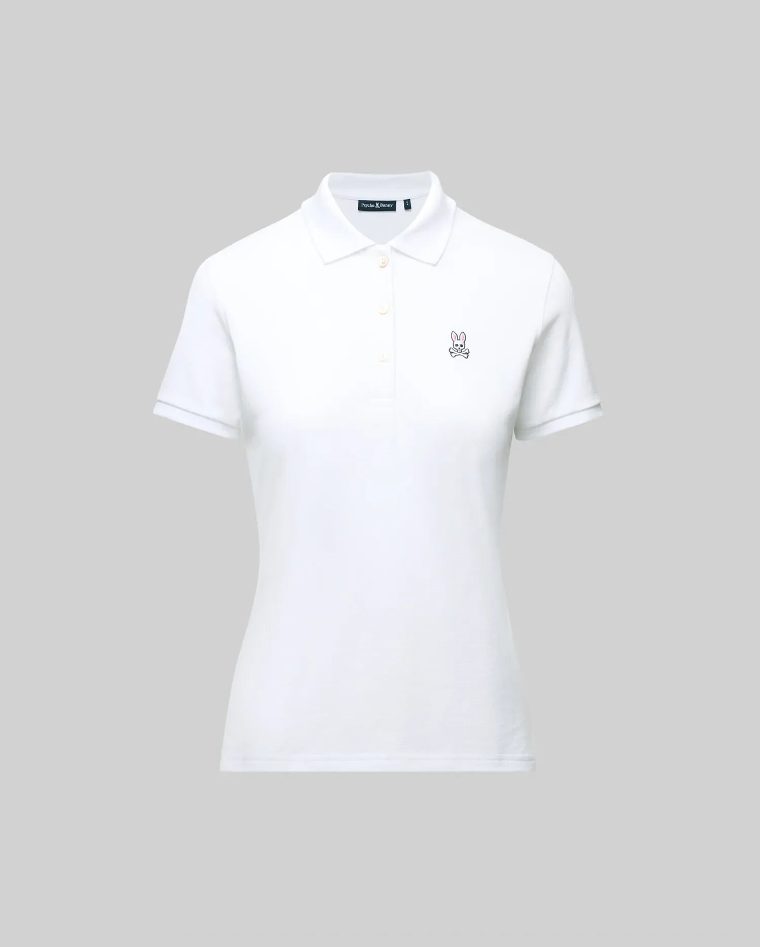 The WOMENS PIQUE POLO - WT0100003 by Psycho Bunny is a white pique polo featuring a collar, buttons, and the embroidered Bunny logo on the left chest. Crafted for Pima flexibility, it is presented against a plain grey background.