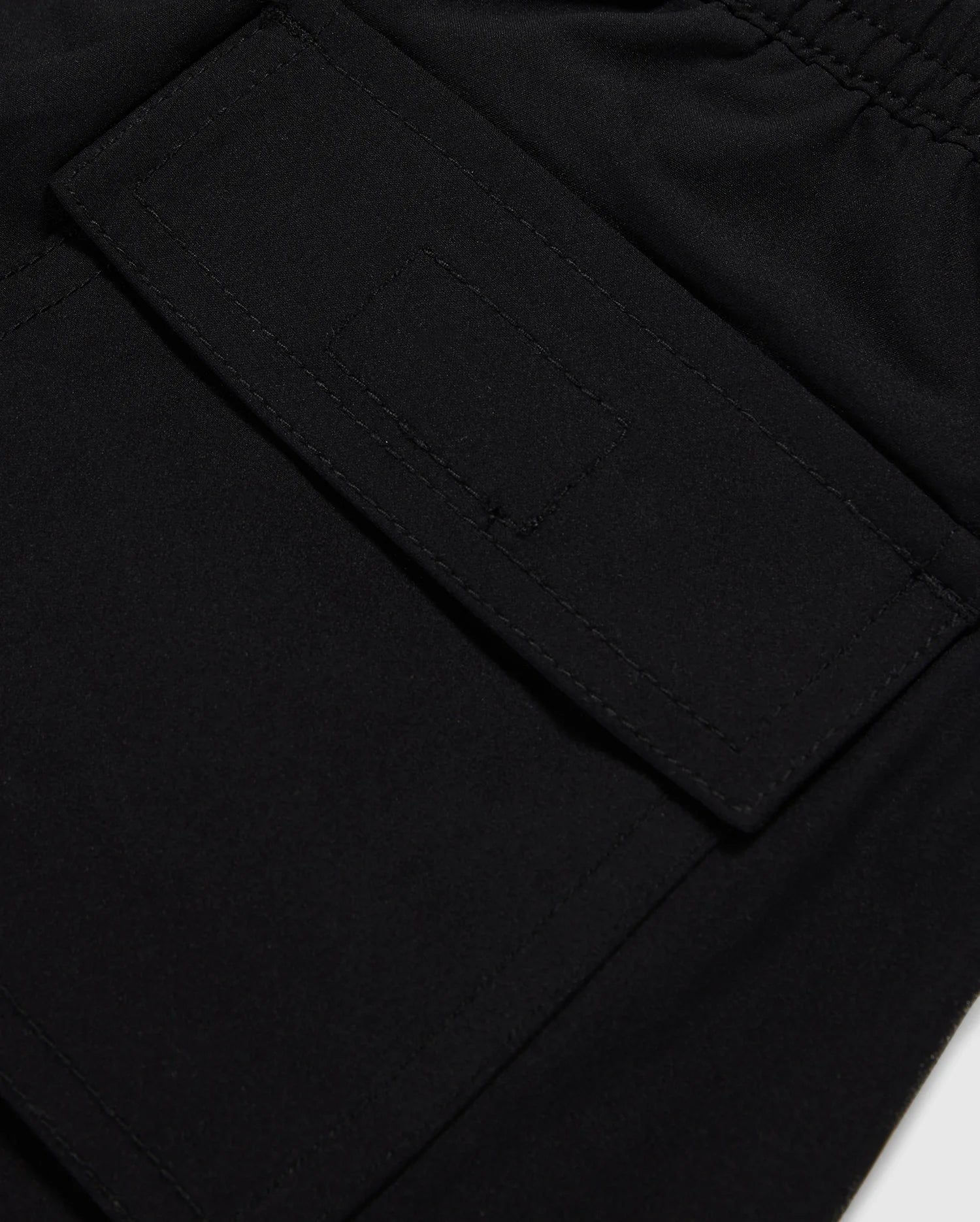 Close-up image of a black fabric pocket with a flap and Velcro closure. The pocket is attached to the KIDS MALTA HYDROCHROMIC SWIM TRUNK - B0W321B2SW by Psycho Bunny, adorned with a playful bunny pattern, and the stitching around the edges is clearly visible. The fabric appears to be smooth and durable.