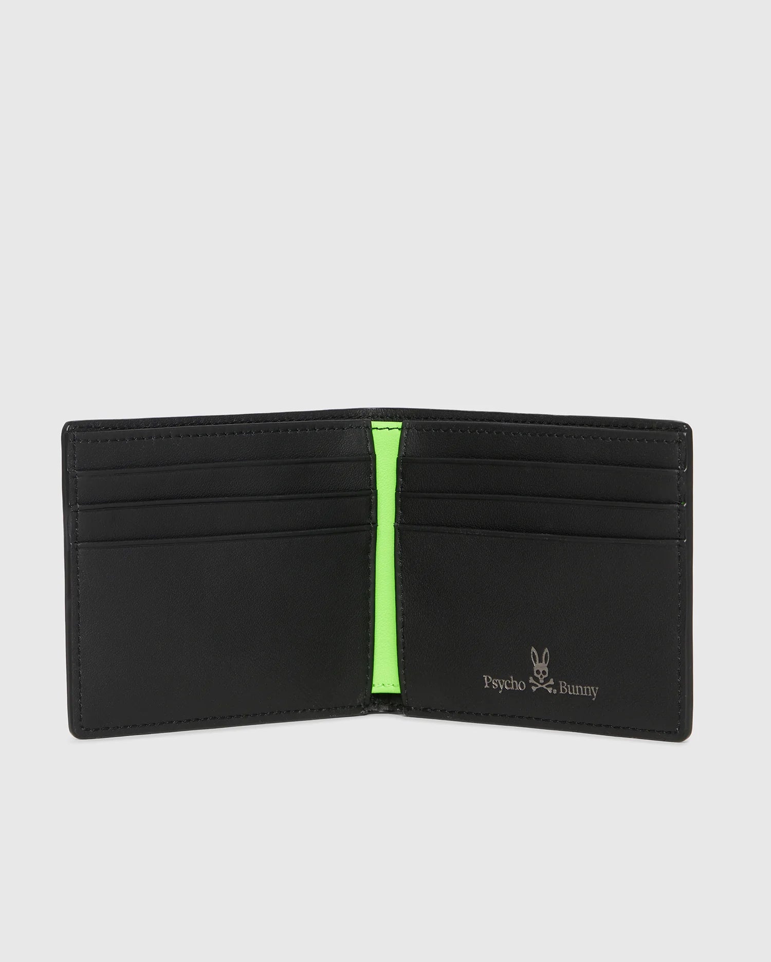 The Psycho Bunny MENS WALLET - B6A403B200 is open, revealing multiple card slots and a neon green accent. Made from grained leather, it features the white Psycho Bunny logo printed on the lower right interior.