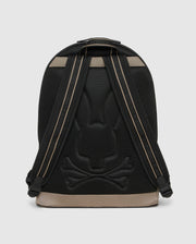 The Psycho Bunny Dome Backpack (B6A628Z1BP) in black and tan is shown from the back, highlighting padded straps, a padded laptop compartment, and a textured bunny head with crossbones on the back panel.