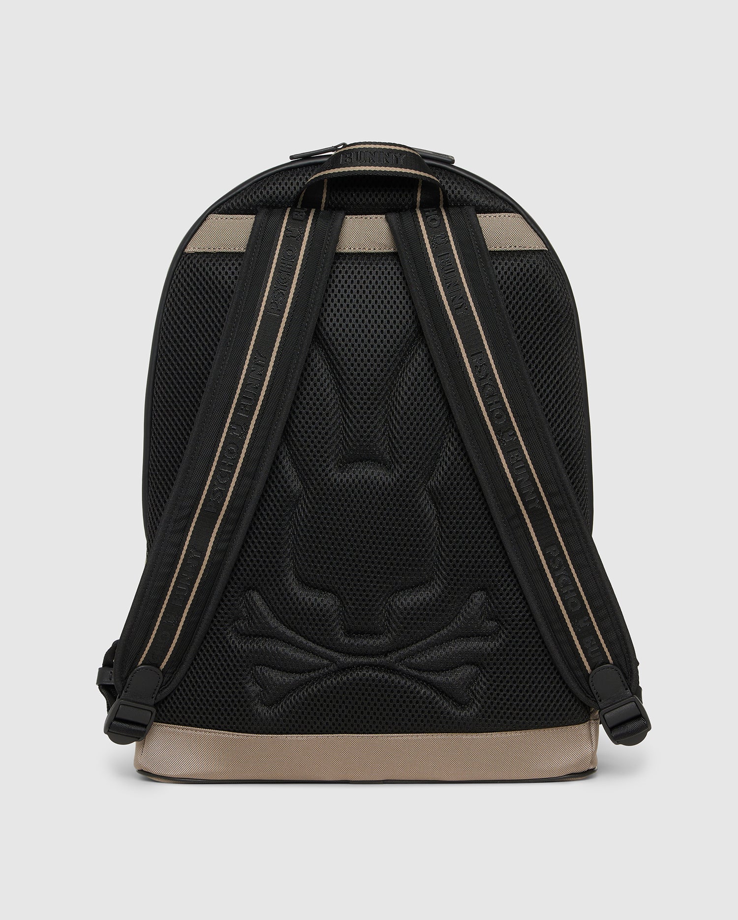 The Psycho Bunny Dome Backpack (B6A628Z1BP) in black and tan is shown from the back, highlighting padded straps, a padded laptop compartment, and a textured bunny head with crossbones on the back panel.