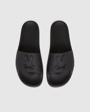 Presenting the Psycho Bunny MENS BUNNY LOGO SLIDES - B6A910U1FT: A pair of black slip-on rubber pool slides boasting a minimalist design. The top straps feature embossed logos with a stylized bunny face and crossed bones beneath. These sandals offer a textured insole and molded footbed for enhanced comfort.