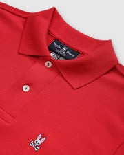 Red Psycho Bunny men's classic piqué polo shirt (B6K001CRPC), made of 100% Pima cotton, features a folded collar and two mother-of-pearl buttons. An embroidered bunny with crossbones decorates the chest. The shirt is displayed on a light gray background.