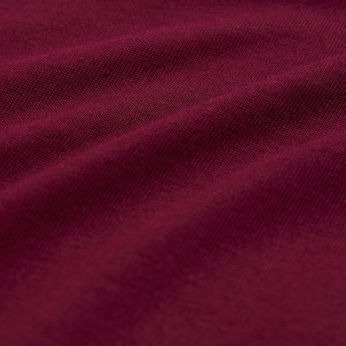 Close-up of maroon fabric with a soft, textured surface that recalls ultra-soft Pima cotton. The lighting highlights gentle folds, evoking depth and richness reminiscent of the Psycho Bunny Men's Classic Crew Neck Tee - B6U014Z1PC.