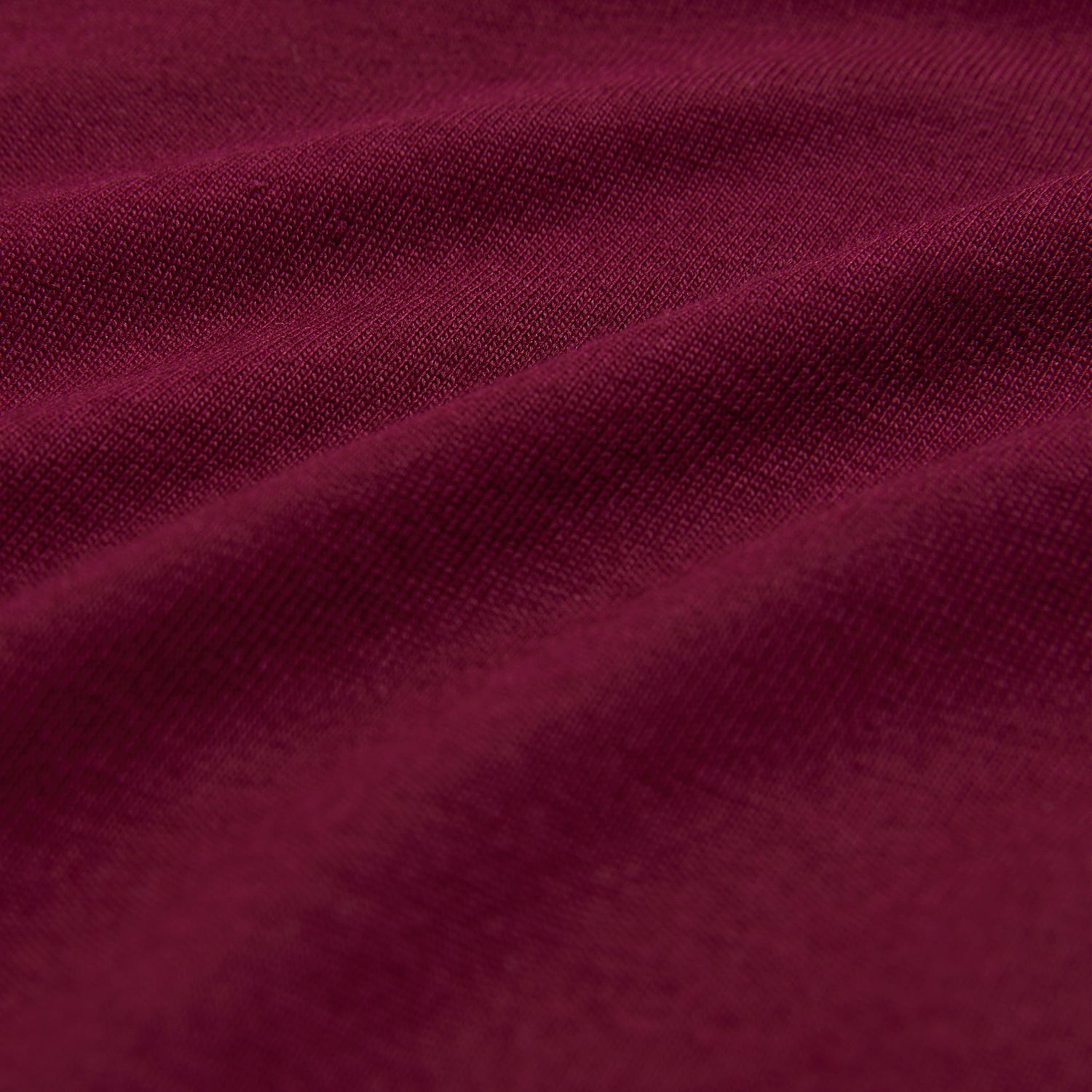 Close-up of maroon fabric with a soft, textured surface that recalls ultra-soft Pima cotton. The lighting highlights gentle folds, evoking depth and richness reminiscent of the Psycho Bunny Men's Classic Crew Neck Tee - B6U014Z1PC.