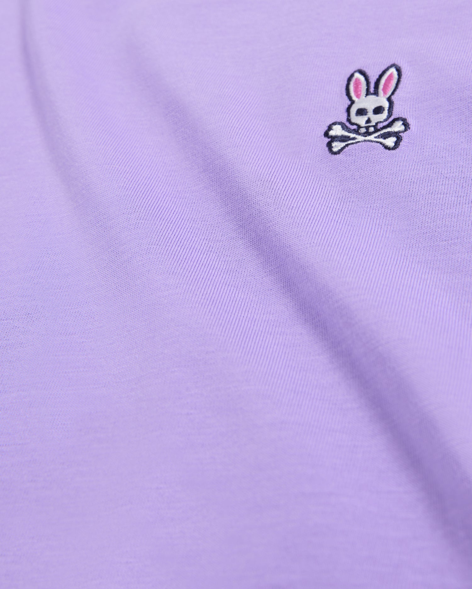 Close-up of the Pima cotton fabric on the Psycho Bunny MENS CLASSIC CREW NECK TEE - B6U014Z1PC, featuring an embroidered Bunny logo with a white skull and crossbones beneath rabbit ears with pink inner ears, located in the upper right area.