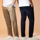 Two people stand side by side against a beige background, each with hands in their pockets. One sports classic-fit khaki pants and white sneakers, while the other wears Psycho Bunny's MENS GABLE REGULAR FIT SPORT PANT - B6P760ARCN in navy blue and white sneakers with green accents. Both are wearing white t-shirts. Their faces are not visible.